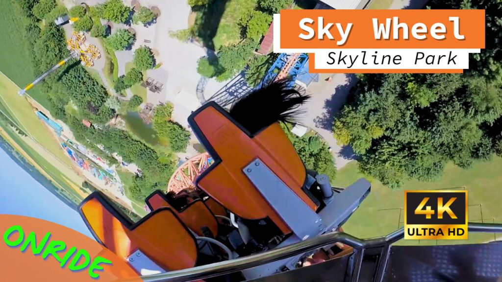 Onride-Perspektive der Achterbahn Sky Wheel im Skyline Park. Der orangefarbene Sitz ist kopfüber geneigt, während die Passagiere senkrecht über dem Boden hängen. Im Hintergrund sieht man aus großer Höhe die Bäume und Wege des Parks. Die Aufnahme ist in 4K Ultra HD-Qualität.