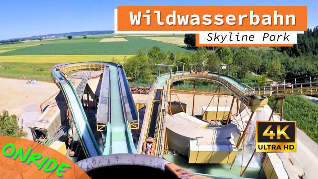 Onride-Perspektive der Wildwasserbahn im Skyline Park. Die grüne Fahrbahn führt über eine steile Abfahrt und mehrere Kurven. Im Hintergrund ist die ländliche Umgebung mit Feldern und Bäumen zu sehen. Die Aufnahme ist in 4K Ultra HD-Qualität und zeigt die Wasserrutsche und die Aufzugskonstruktion.