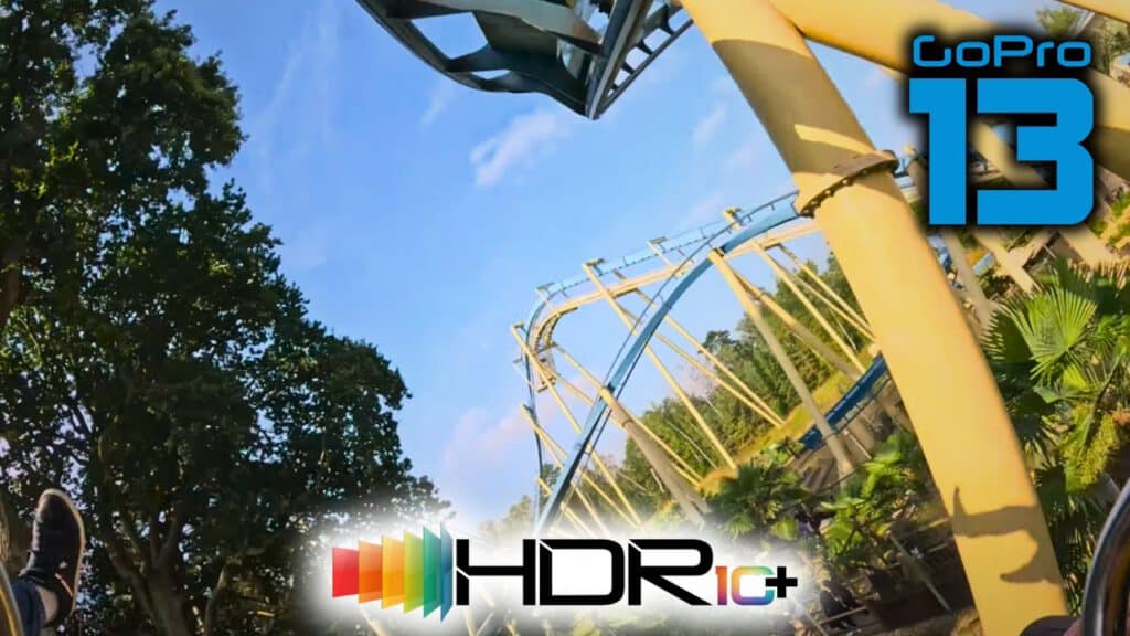 Eine Onride-Perspektive auf der Achterbahn „OzIris“ im Parc Astérix, aufgenommen mit der GoPro HERO 13 in HDR10+. Die Schienen der Inverted-Achterbahn sind in Blau- und Gelbtönen gehalten und führen durch eine Baumlandschaft, während der Himmel im Hintergrund leuchtet. Das GoPro HERO 13 und HDR10+ Logo sind im Bild zu sehen.