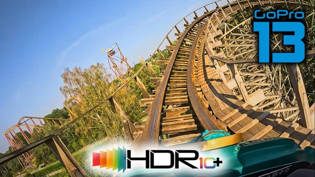 Eine Front-Row-Perspektive auf der Holzachterbahn „Tonnerre 2 Zeus“ im Parc Astérix, aufgenommen mit der GoPro HERO 13 in HDR10+. Die hölzerne Struktur der Bahn windet sich durch eine Kurve, umgeben von Bäumen und einem klaren blauen Himmel. Im Vordergrund das HDR10+ und GoPro HERO 13 Logo.