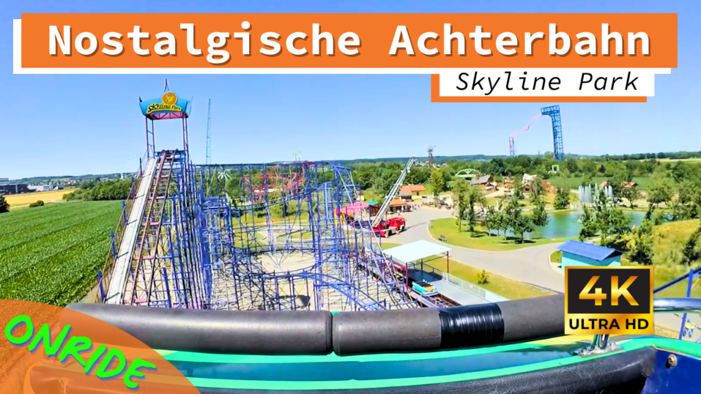 Blick auf die nostalgische Achterbahn im Skyline Park aus der Onride-Perspektive. Die Bahn besteht aus blauen Metallstrukturen und bietet steile Auf- und Abfahrten. Im Hintergrund sind weitere Attraktionen und die grüne Parklandschaft zu sehen. Ein "Skyline Park"-Schild sowie ein Hinweis auf die 4K Ultra HD-Qualität sind ebenfalls sichtbar.